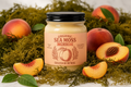 A jar of Organic Sea Moss Peach flavor, created by D'Nese, styled on a light marble surface with fresh peach slices, whole peaches, and green leaves. The jar has a black lid and a peach-colored label with illustrations of a peach and wheat.